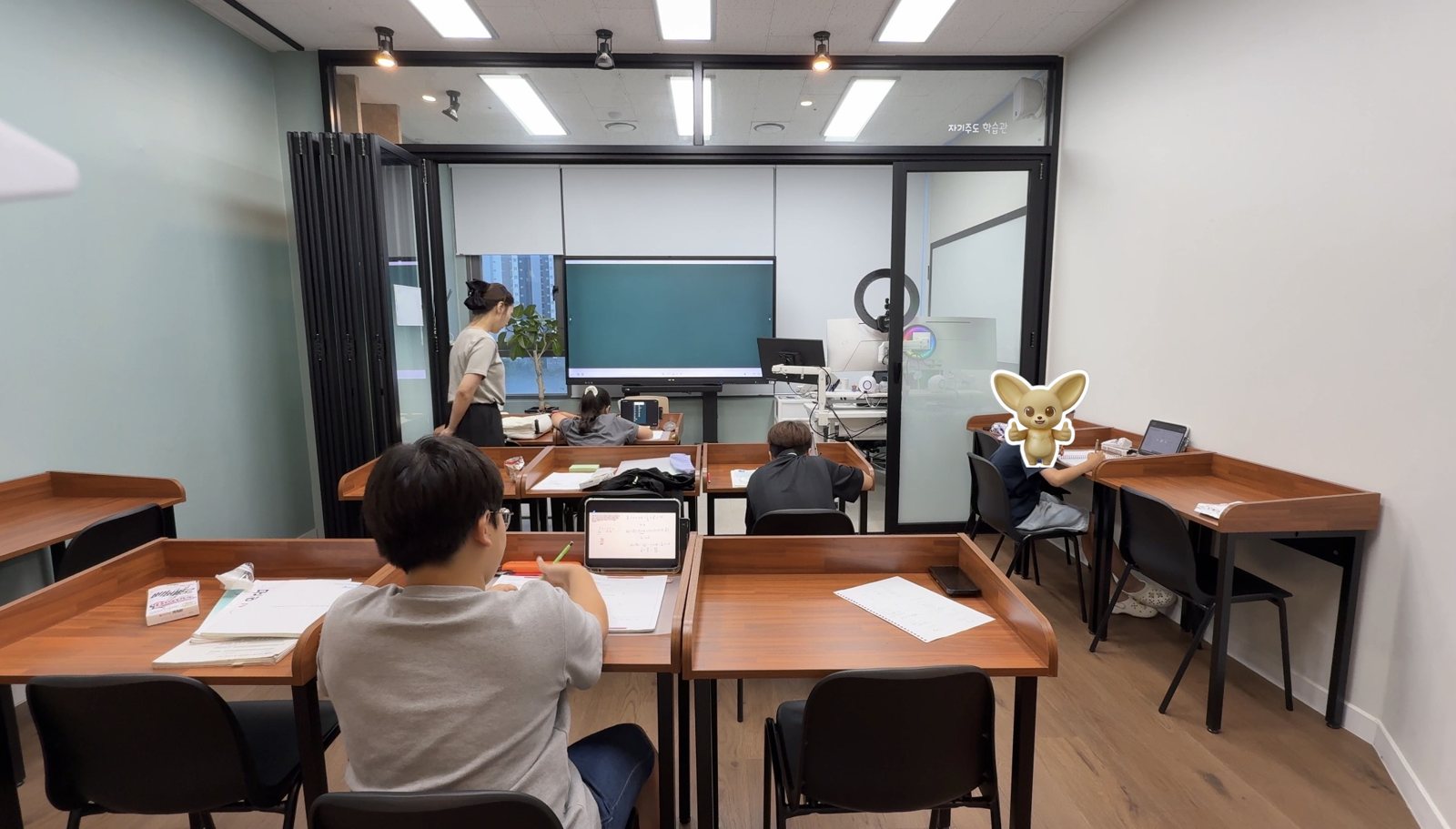 배곧캠퍼스 교실: 전자칠판 앞에서 학생들이 각자 책상에서 문제를 푸는 모습